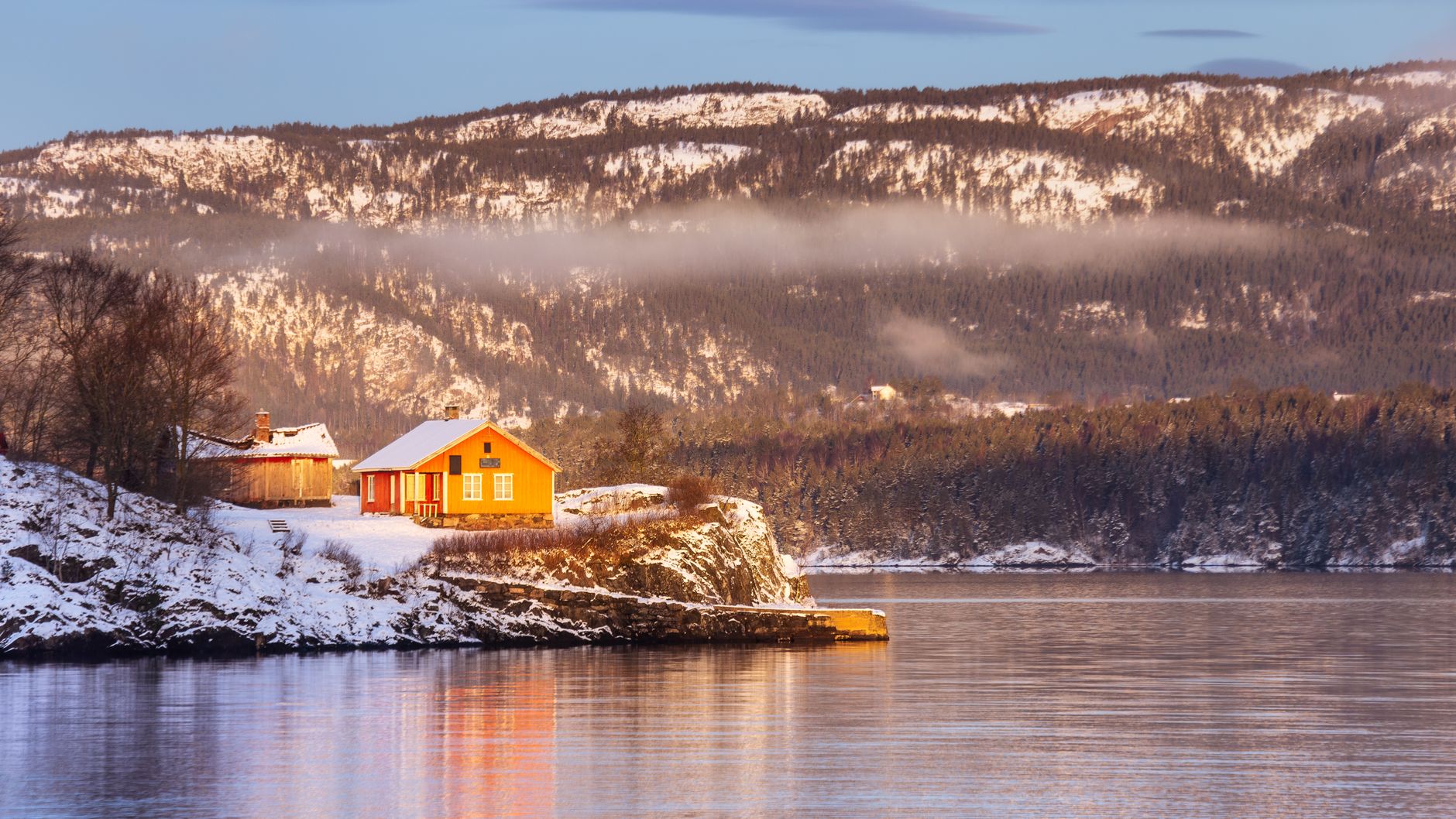 Modern wooden cabin overlooking snowy fjord landscape